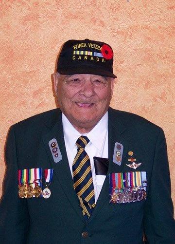 Elderly man in military uniform with medals and cap, smiling.