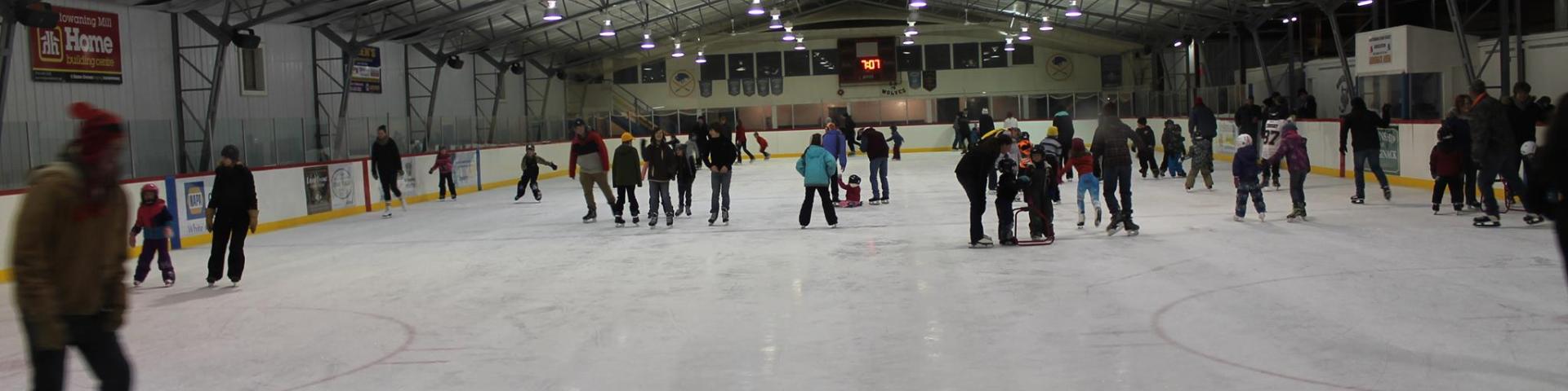An indoor ice skating rink filled with skaters of all ages on the ice.
