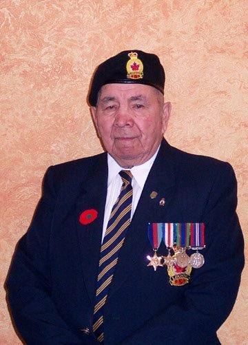 Elderly man in a uniform with a beret and medals against a textured wall.
