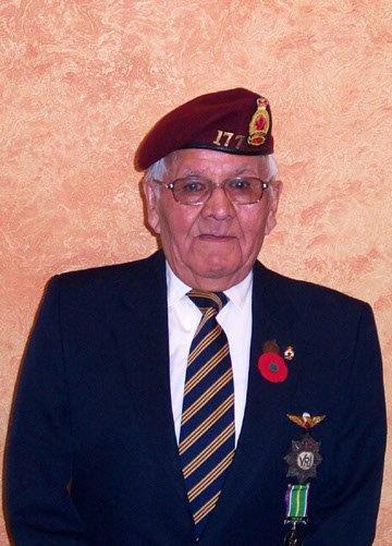 Elderly man in military uniform with medals and maroon beret, smiling slightly.