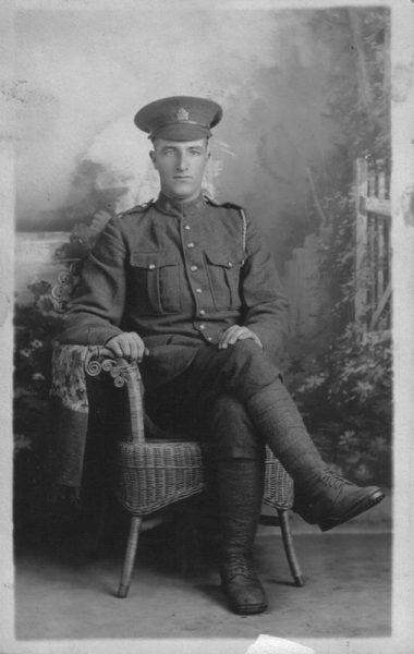 Young soldier in uniform seated on wicker chair, formal portrait.