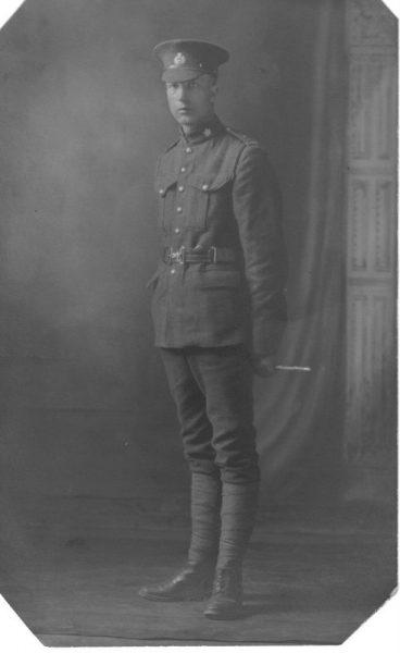 Sepia-toned photo of a soldier in uniform with a cap, standing in a studio setting.