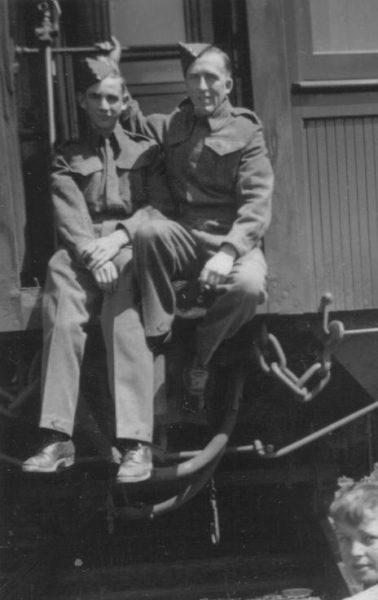 Two soldiers sitting on a train step, wearing uniforms and caps, black and white photo.