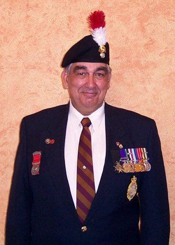 Elderly man in a suit with medals, wearing a beret with a red plume.