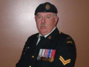 Man in military uniform with medals, standing against a brown background.