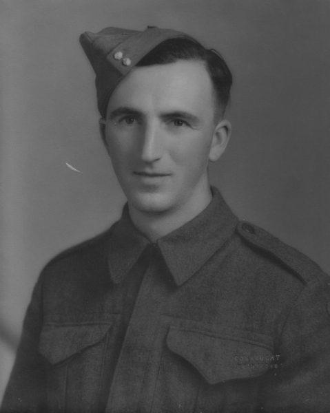 Black and white photo of a soldier in uniform and cap, looking at the camera.
