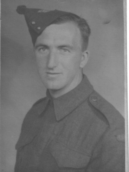 Black and white photo of a soldier in uniform and cap, looking at the camera.
