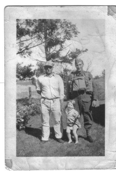 Two men and a child standing outside in a garden, black and white photograph.