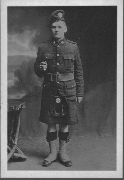Young man in military uniform with kilt, standing in a studio.