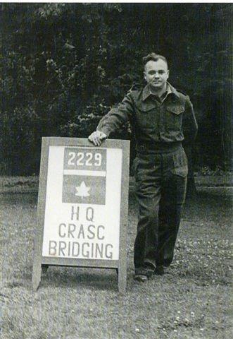 Man in military uniform standing beside a sign with "HQ CRASC Bridging" on it.