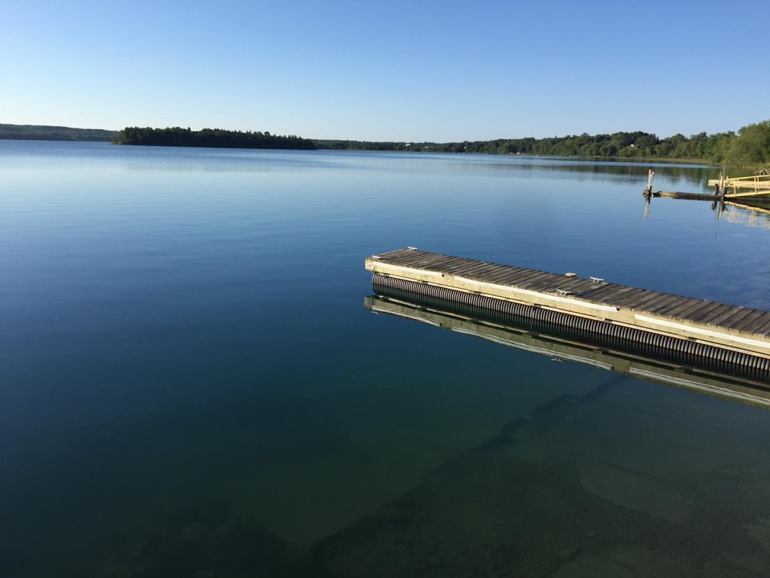 Calm lake with a wooden dock under a clear blue sky.
