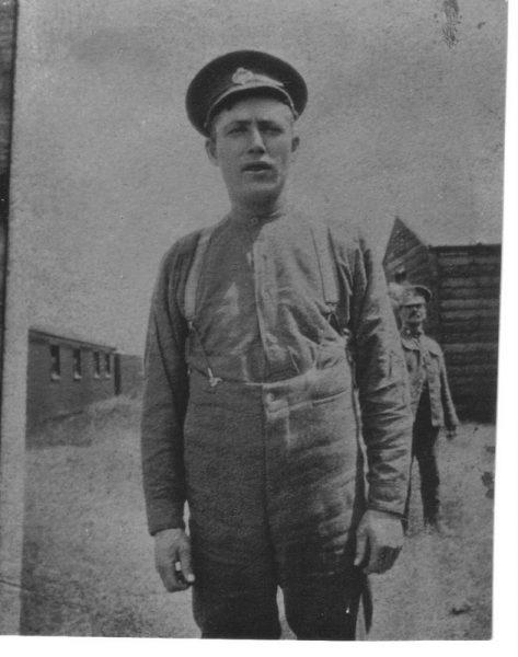 Black and white photo of a man in uniform outdoors, with buildings in the background.