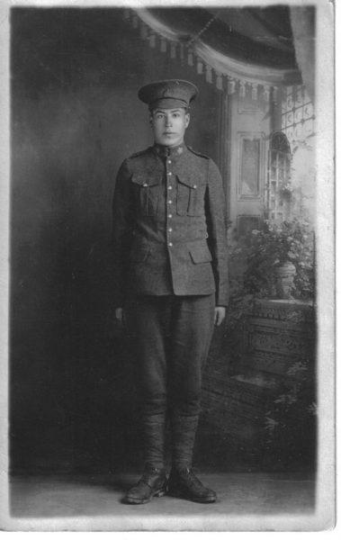 Young soldier in uniform standing indoors, early 20th-century attire. Black and white photo.