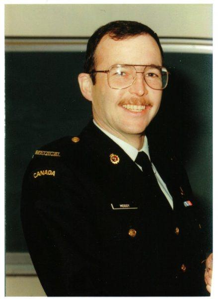 Man smiling in a military uniform with medals, in front of a dark board.