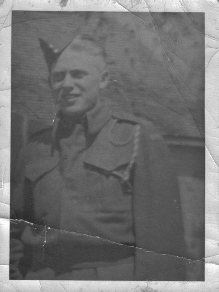 Black and white photo of a soldier in uniform with a peaked cap, smiling.