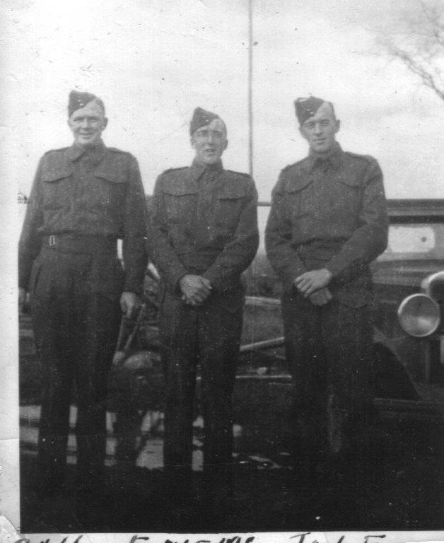 Three soldiers in uniform stand side by side, posing in front of a vintage car.