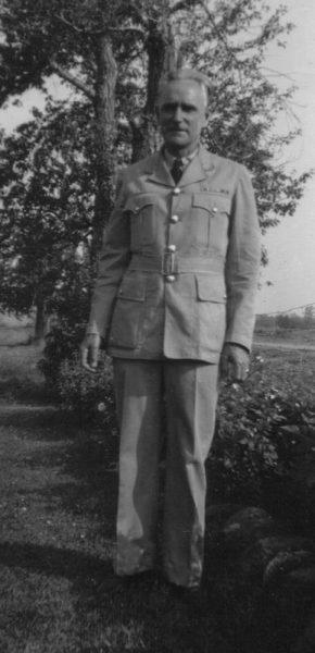 Man in military uniform standing outdoors, trees in the background. Black and white photo.