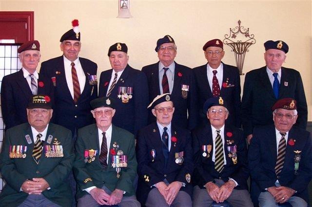 Eleven elderly veterans in uniform, some wearing medals and hats, posed in a room.