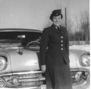 Smiling person in uniform stands by a vintage car in snowy setting.