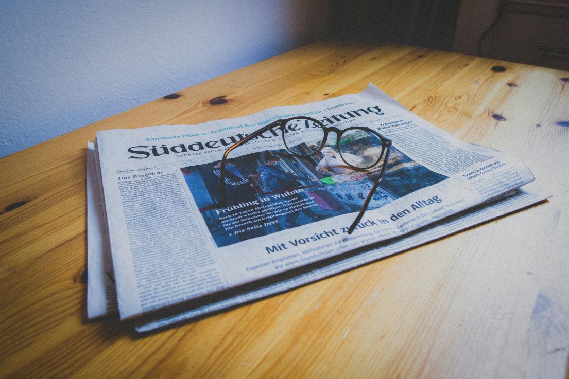 Newspaper with glasses on a wooden table.