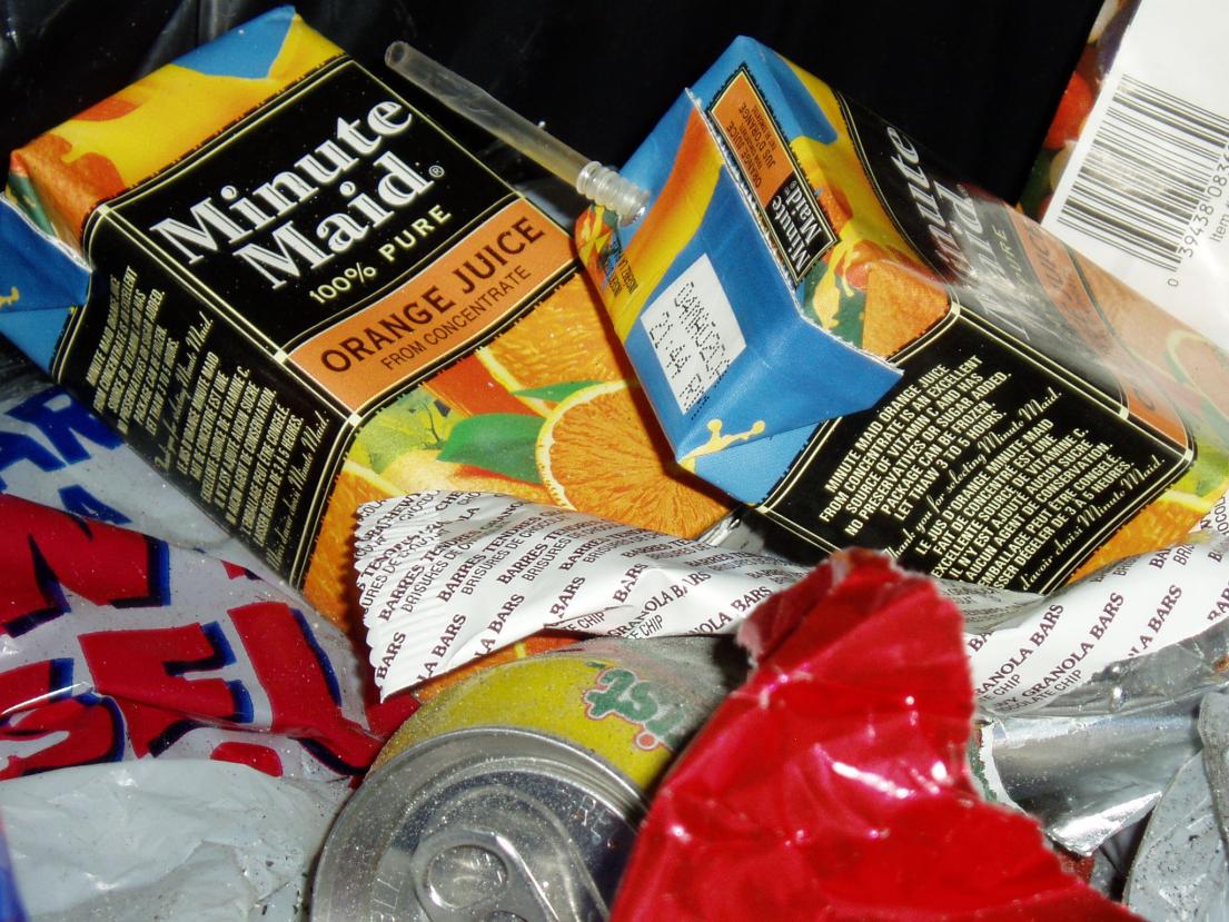 Empty juice cartons and cans in a pile of trash.