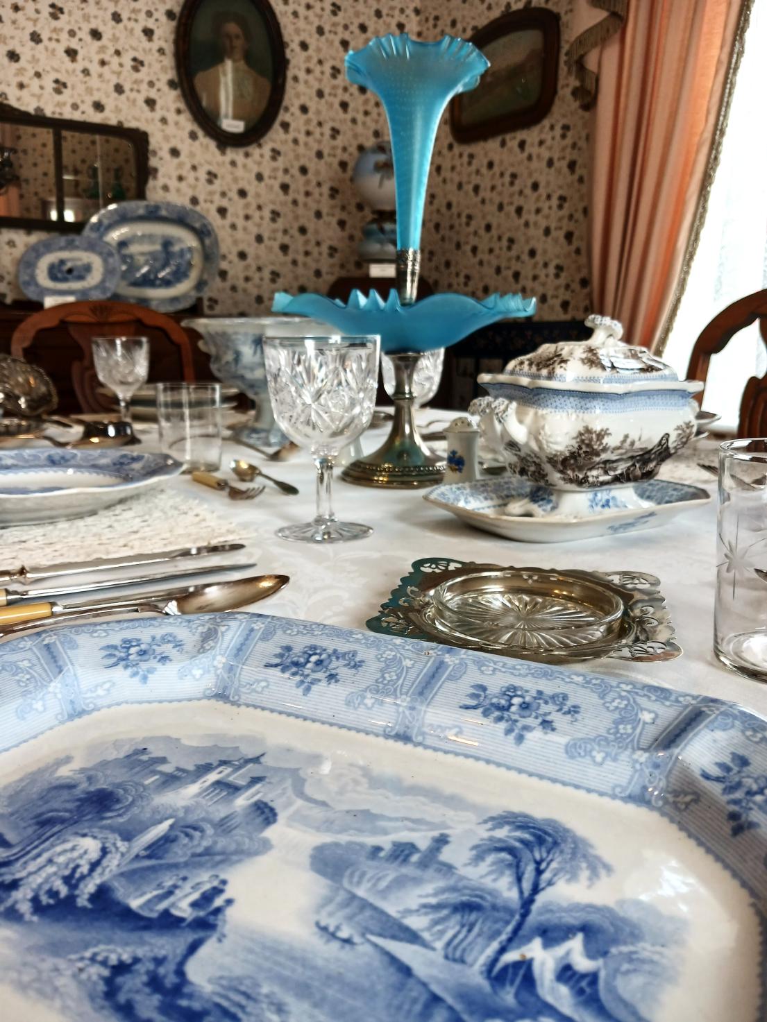 a dining room table set with antique blue and white dishes in a historic setting with a turquoise blue epergne in the centre of the table.  