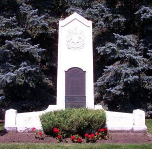 White stone monument surrounded by trees and red flowers.